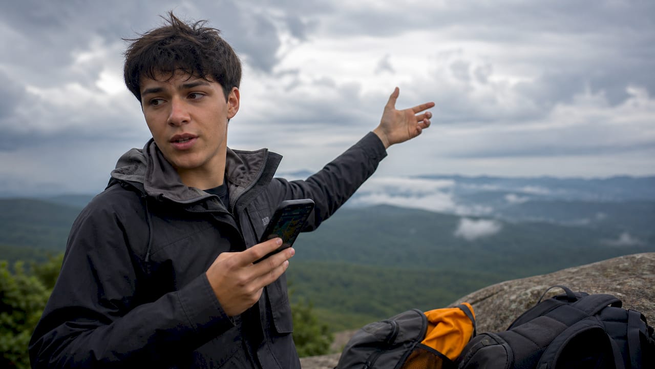 student pointing at cloudy sky with weather app